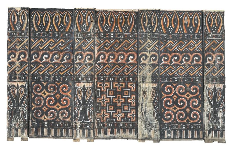An authentic antique Toraja tribal wood carving panel from Sulawesi, featuring hand-painted geometric motifs, traditional spirals, and stylized buffalo head carvings in red, black, and white.