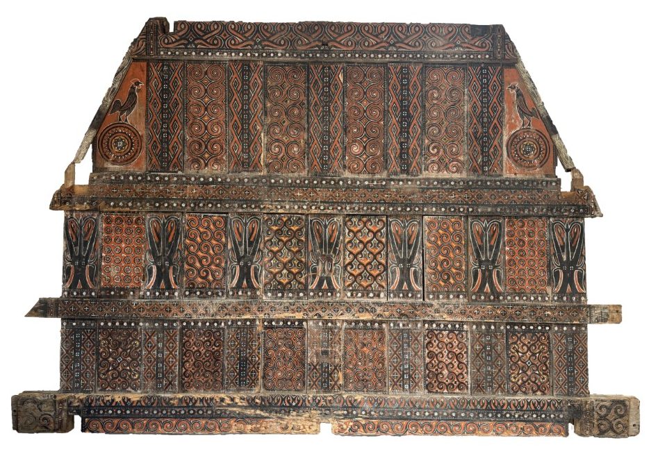 An authentic, intricately hand-carved antique wooden gable panel from a Toraja Tongkonan house in Sulawesi, featuring traditional red, black, and yellow tribal motifs.